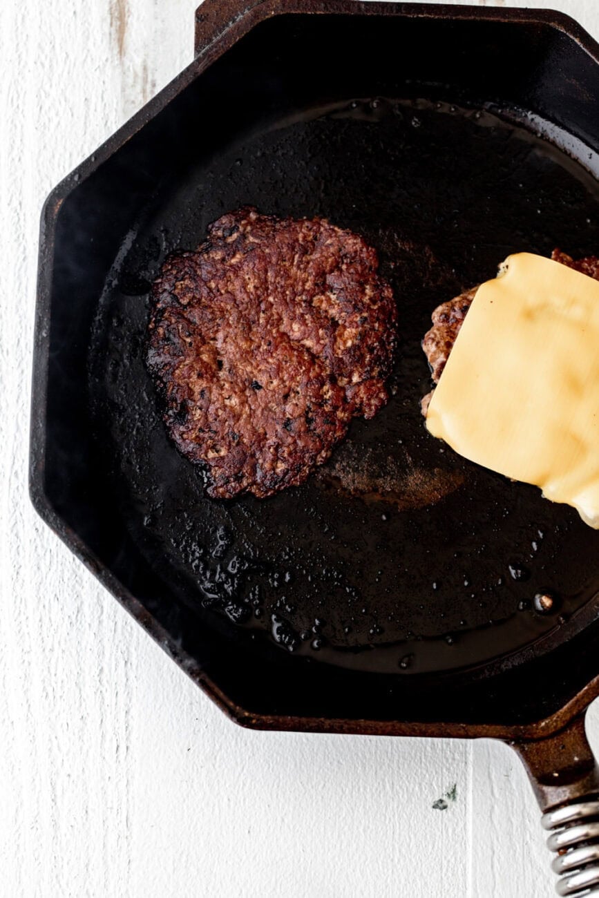smash burger patties seared with crust and american cheese in cast iron pan.