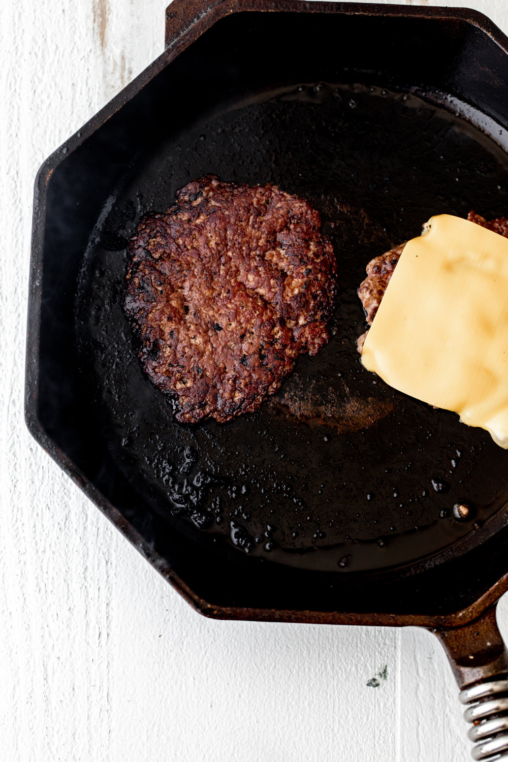 smash burger patties seared with crust and american cheese in cast iron pan
