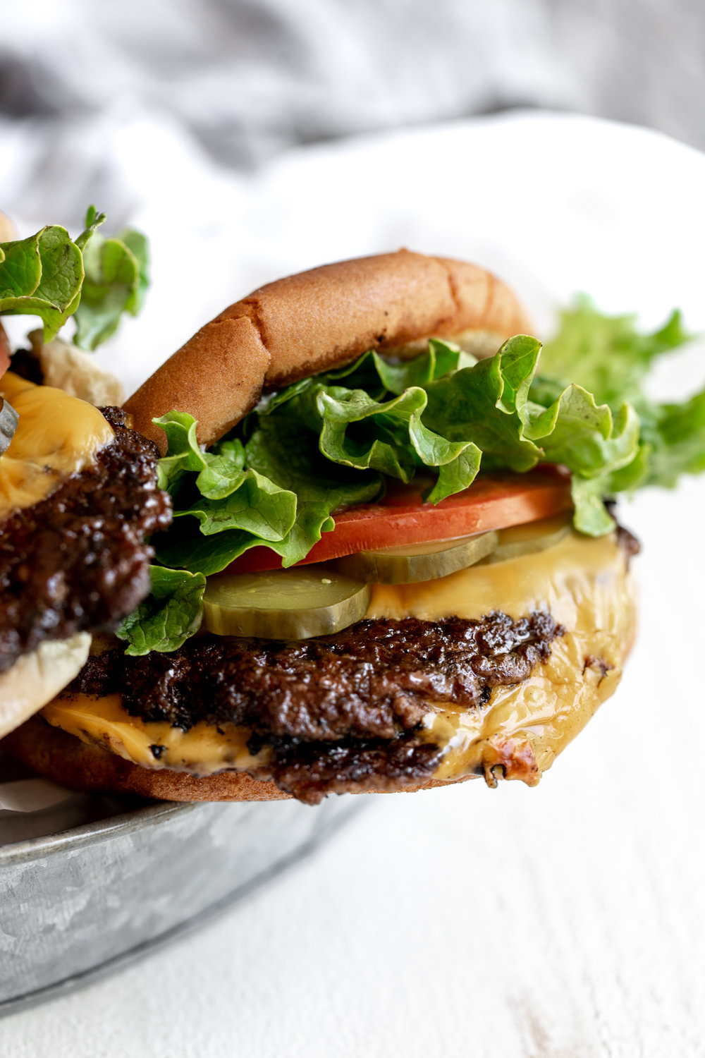 smashed burgers on potato hamburger buns with green leaf lettuce, tomato slice and pickles