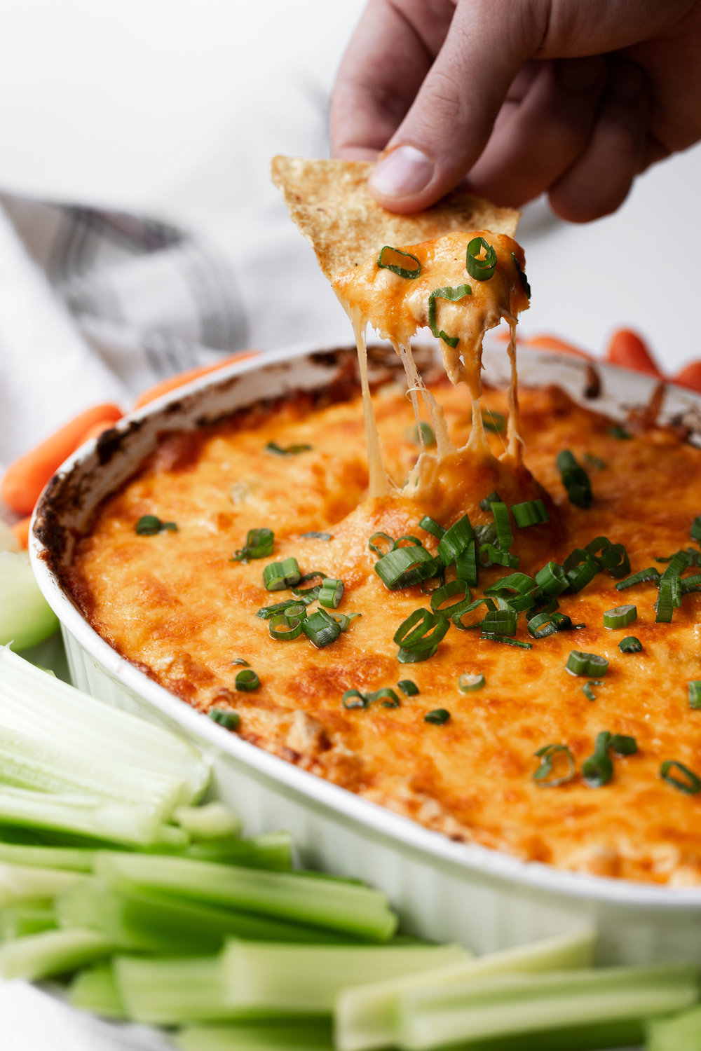 buffalo chicken dip recipe closeup with tortilla chip partly in the dip and a hand pulling it showing a cheese pull