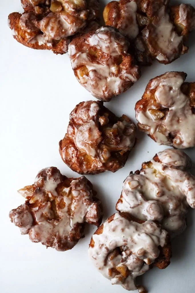 fried apple fritters recipe with cider glaze arranged on white background.