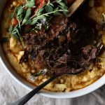 braised short rib with chilies over charred corn polenta in a white serving bowl on a grey napkin