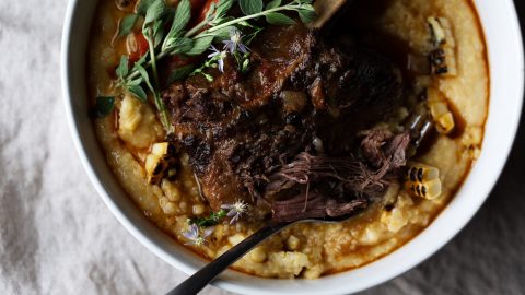 braised short rib with chilies over charred corn polenta in a white serving bowl on a grey napkin