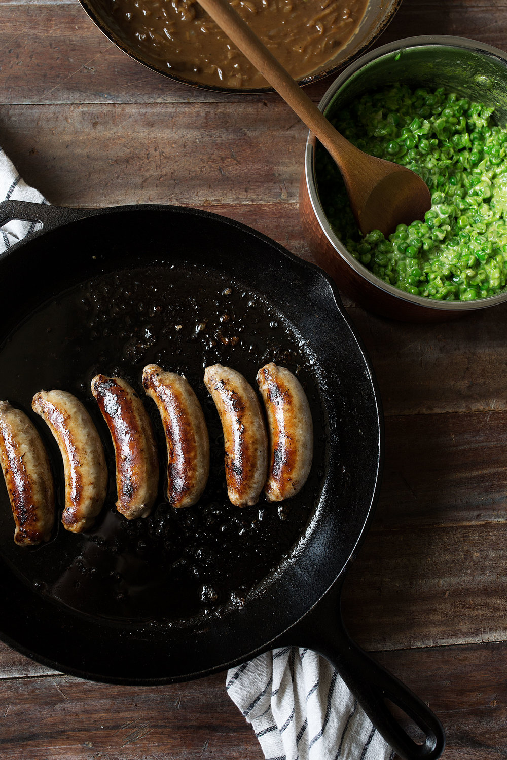cooked bangers in cast iron pan with mushy peas
