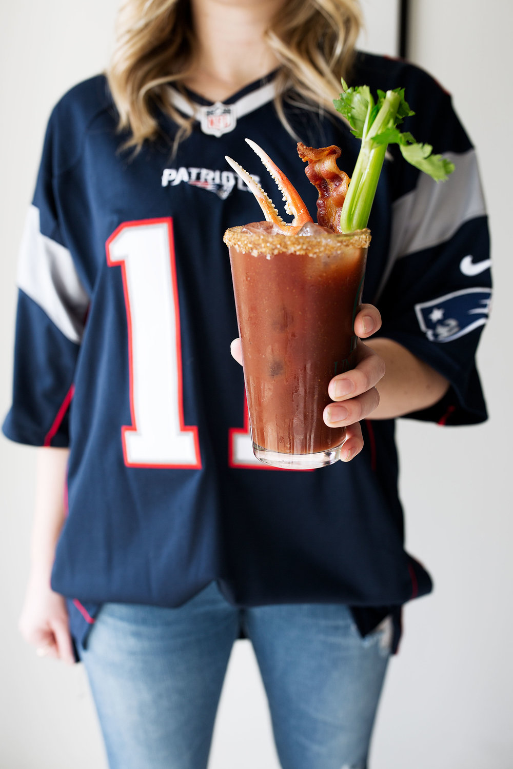 loaded old bay bloody mary with candied bacon and snow crab claw with celery and patriots football jersey