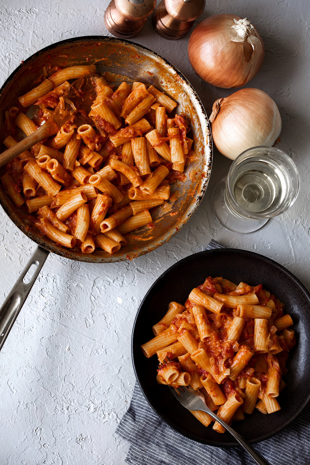 spicy rigatoni in sauté pan with creamy red sauce and whole onions on side