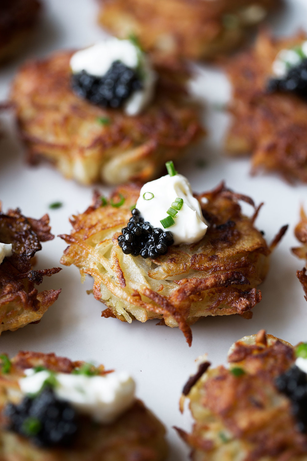 closeup of mini bougie latkes with crispy golden brown crust of shredded potatoes topped with caviar,  creme fraiche and chives