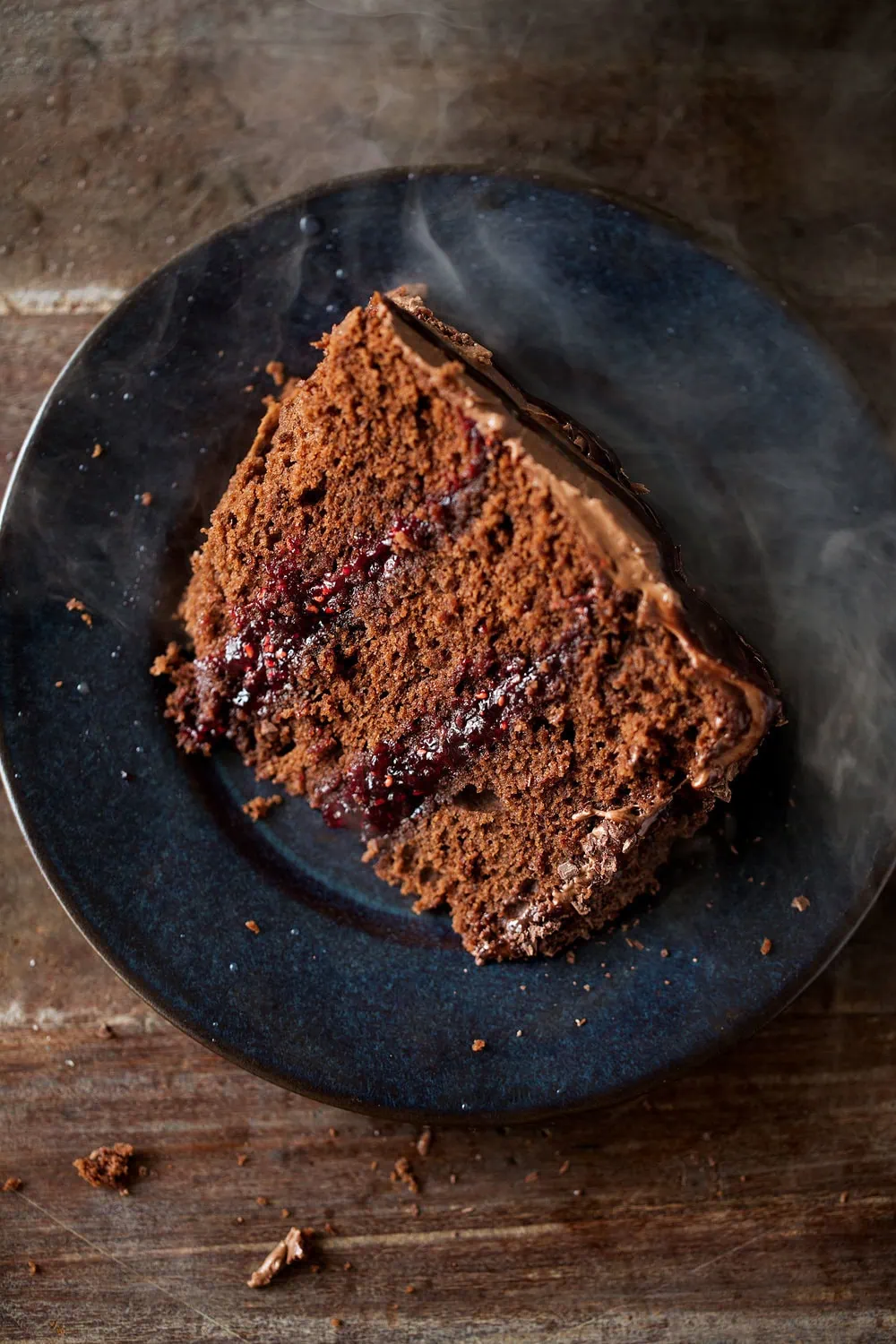Dark Chocolate halloween Cake with Raspberry Filling, Chocolate Ganache slice of cake on black plate with spooky smoke