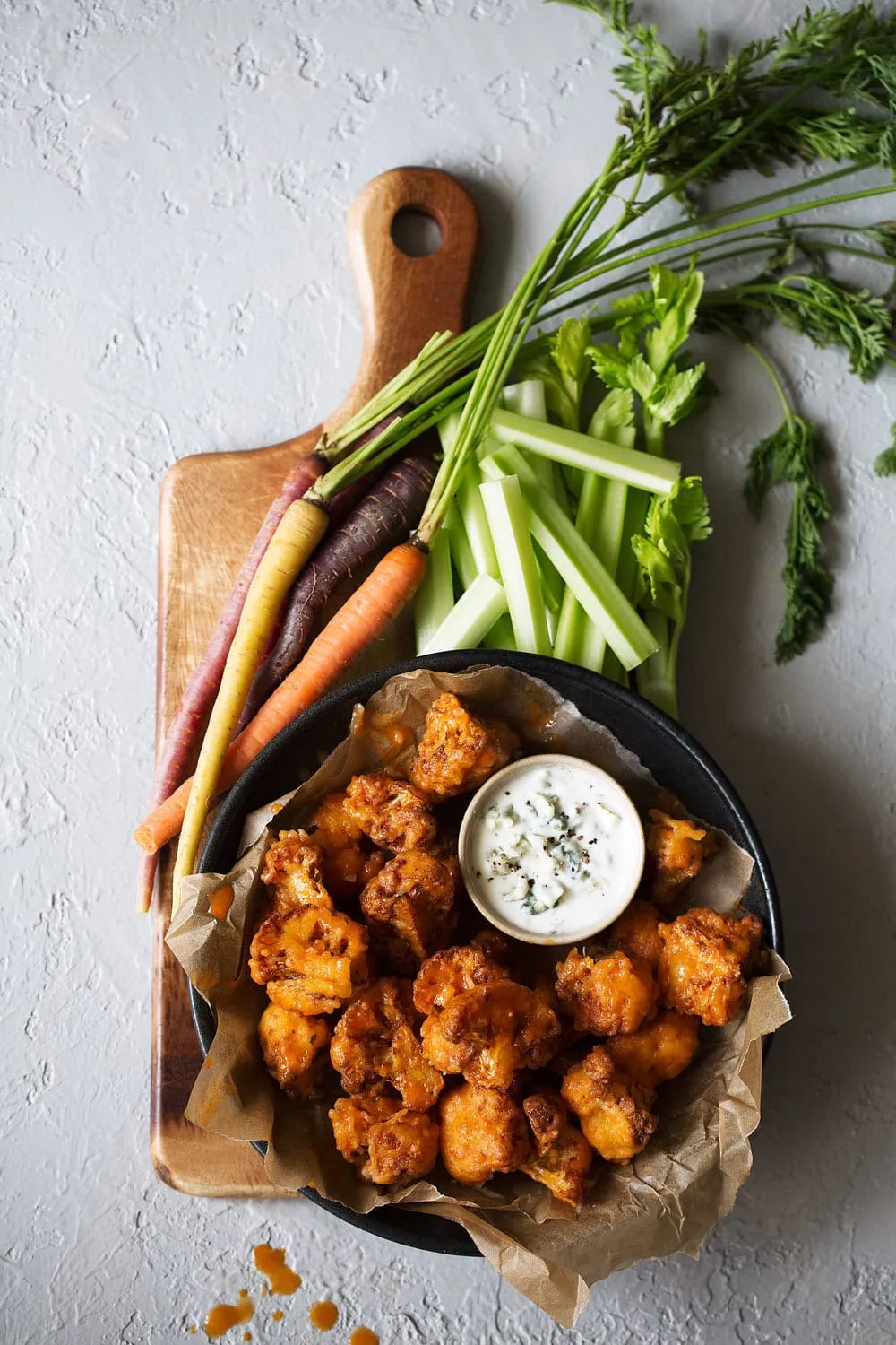 Crispy Buffalo Cauliflower Bites on cutting board with blue cheese dressing carrots and celery