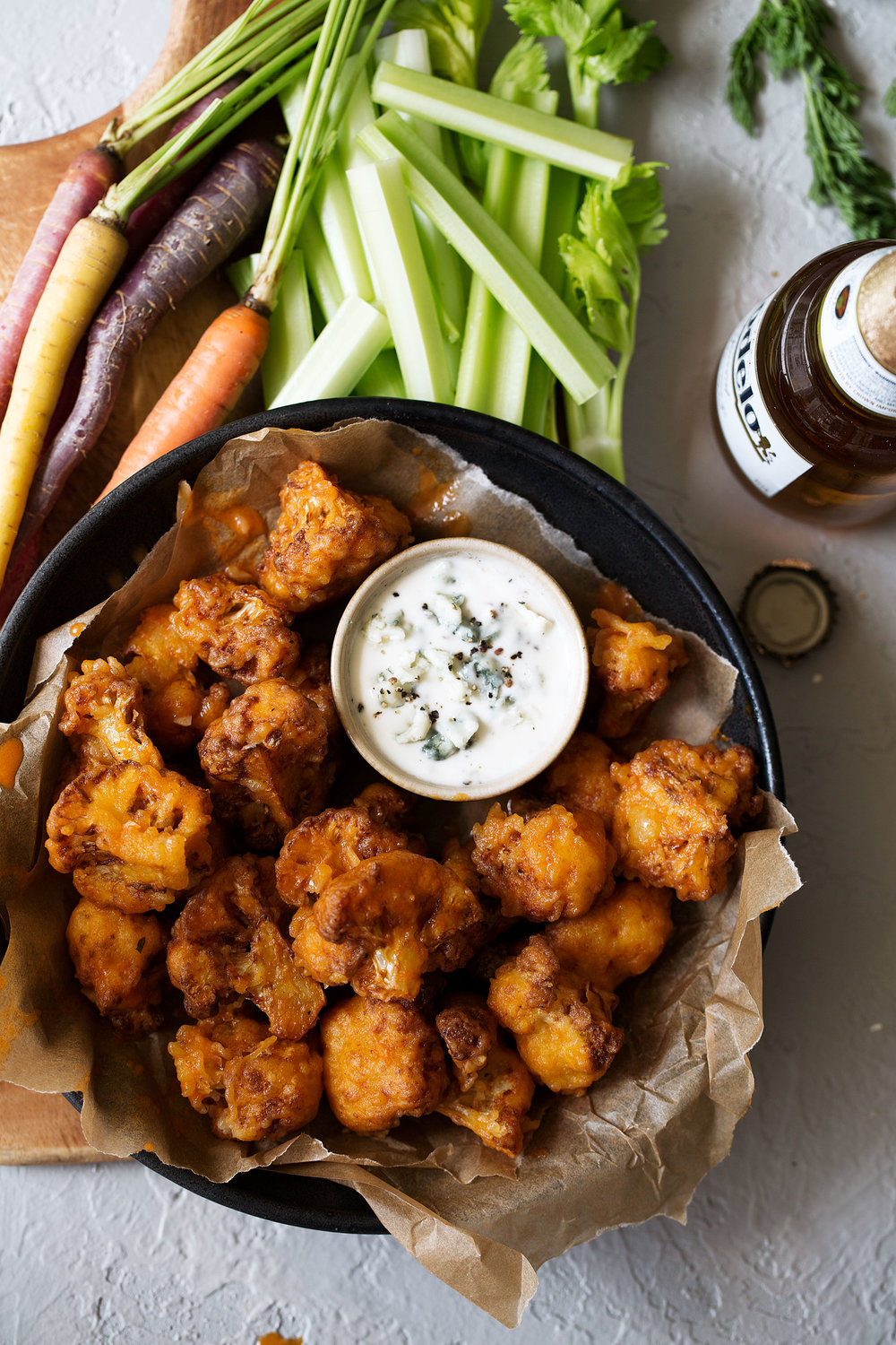 Crispy Buffalo Cauliflower Bites on cutting board with blue cheese dressing vegetables for dipping