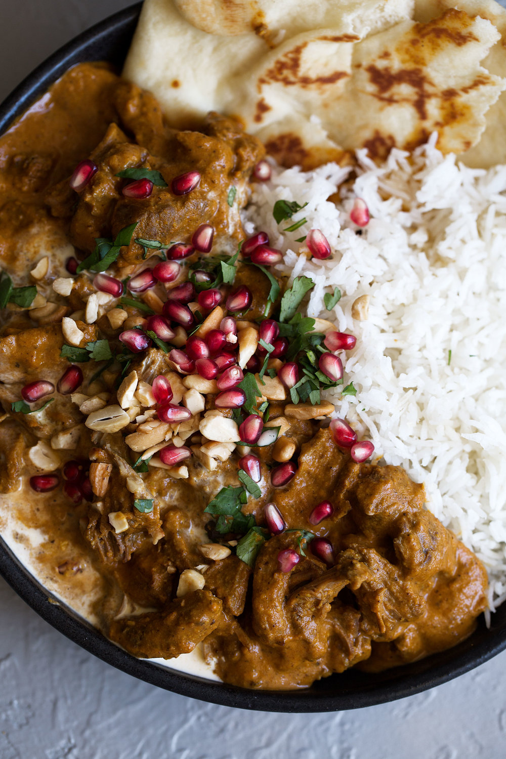 lamb korma recipe over white rice with naan bread garnished with cilantro pomegranate seeds and nuts