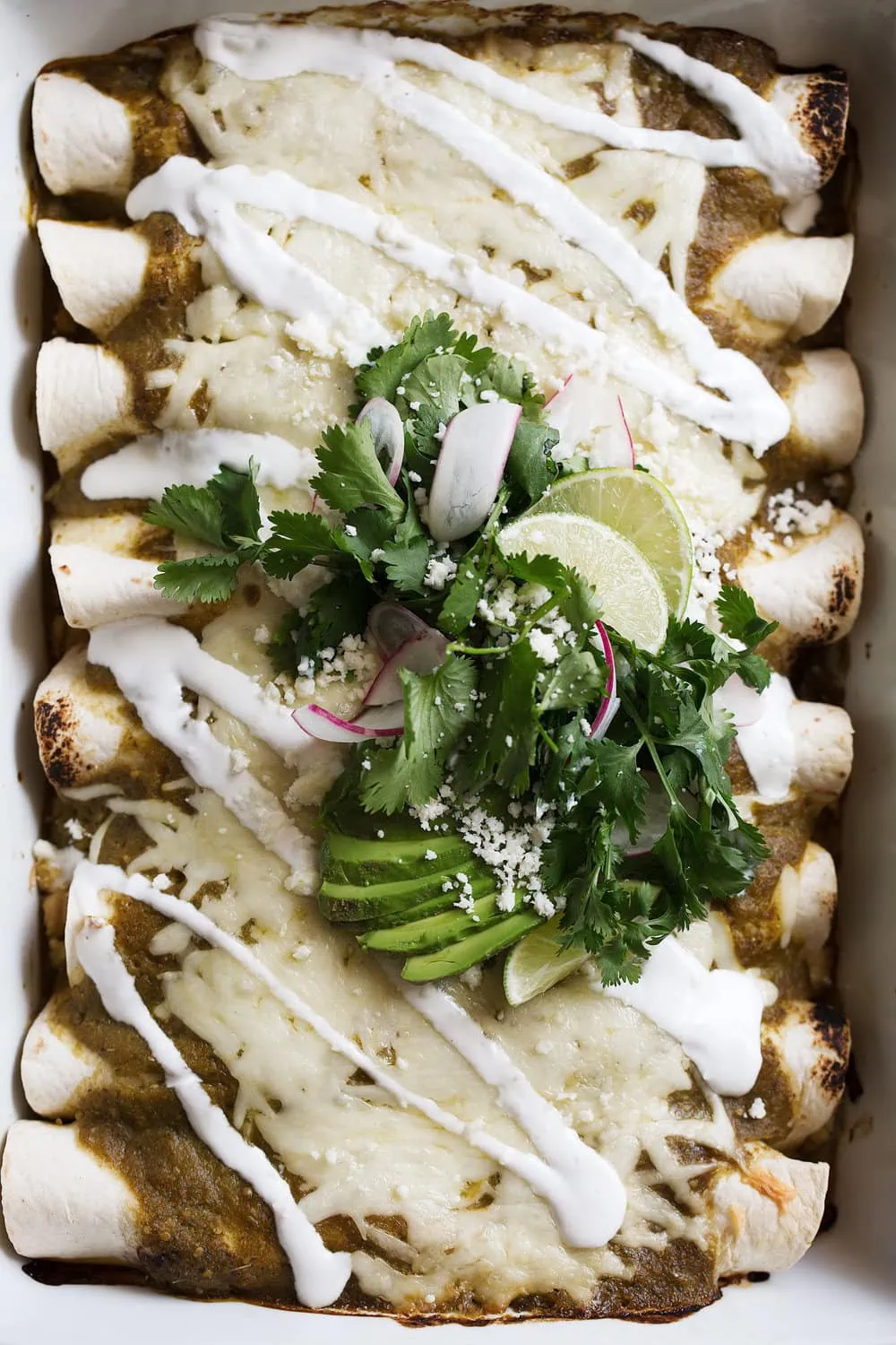 cheesy chicken & sweet corn enchilada verdes in pan with avocado sour cream and cilantro