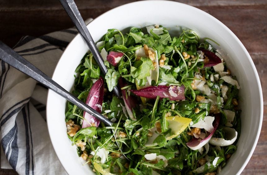 arugula and endive salad in salad bowl with serving spoons.