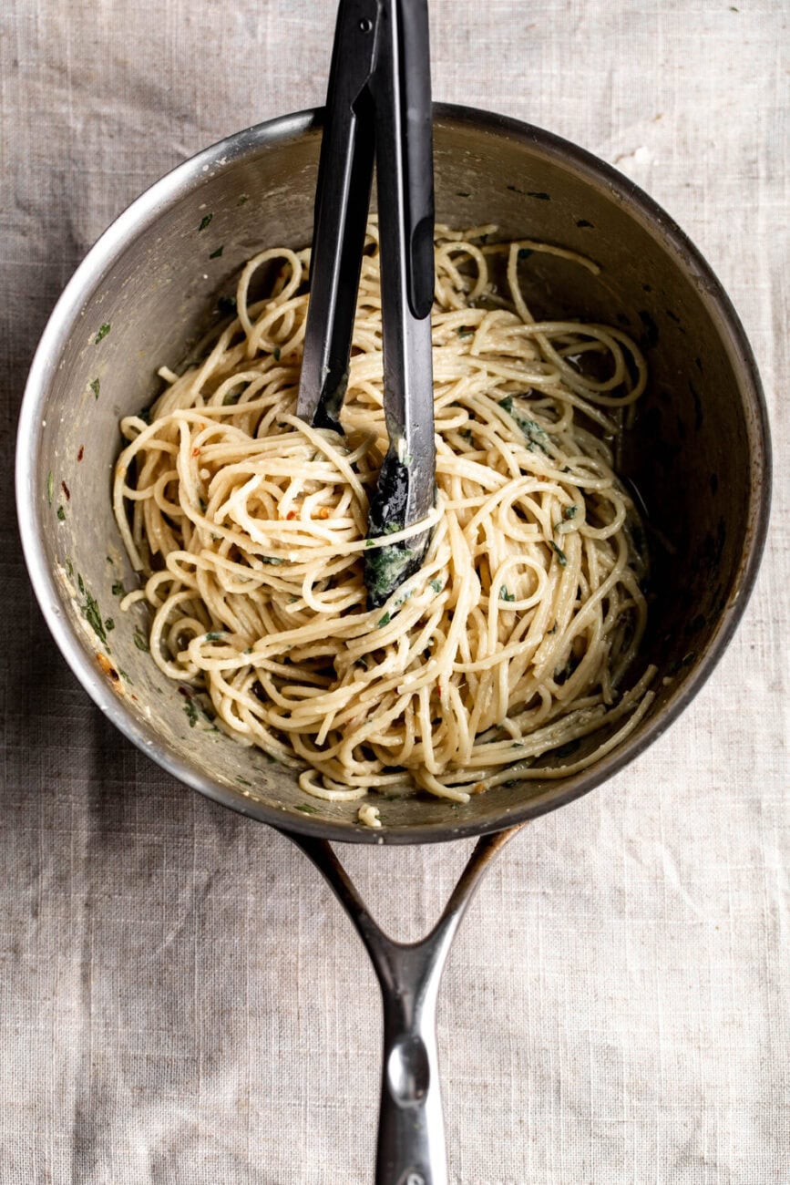 simple roasted garlic pasta twisted in tongs in pot.