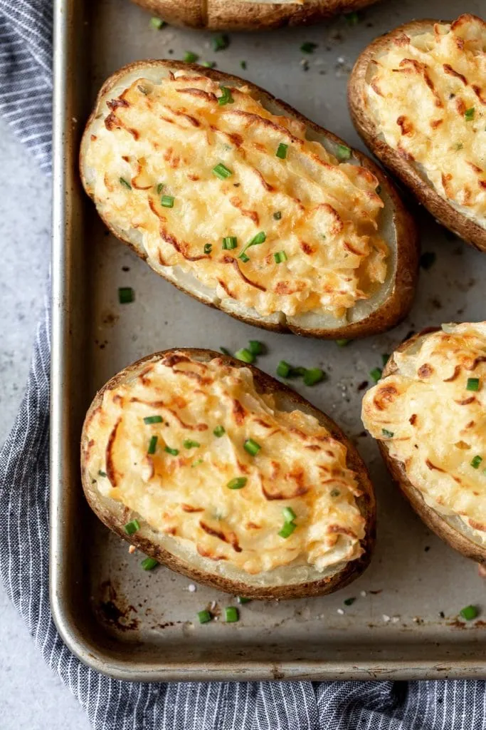 cheesy cheddar twice baked russet potatoes garnished with chives on baking sheet