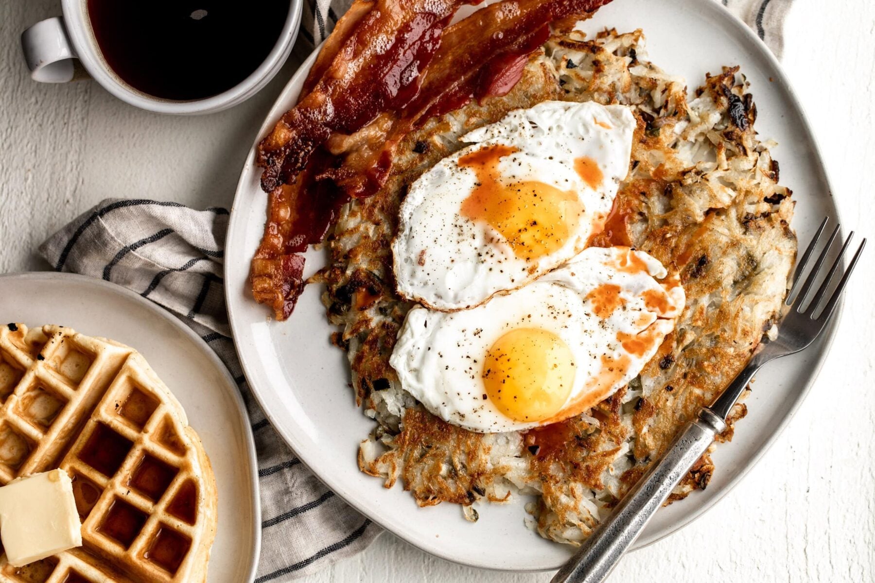 Jalapeno hash browns with eggs on top and bacon on the side.