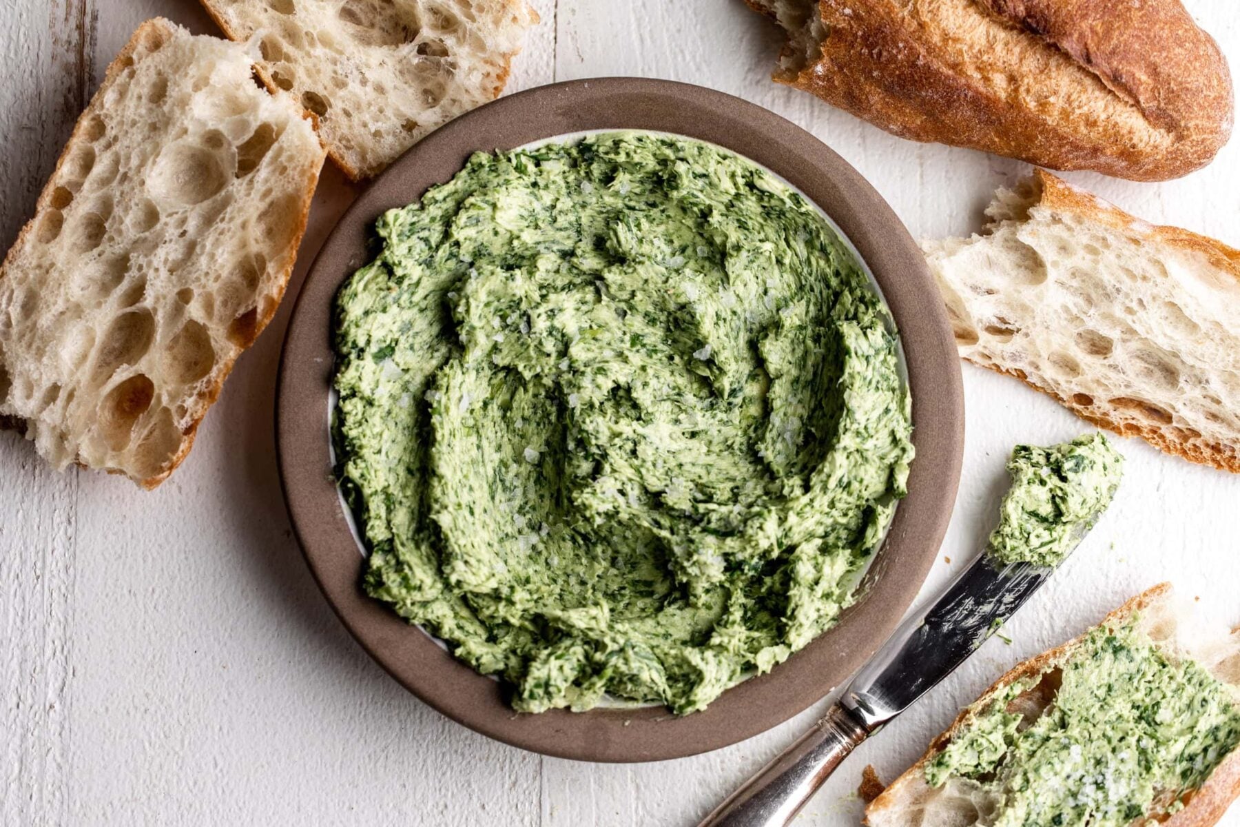 green ramps blended into butter with sliced baguette on white wood.