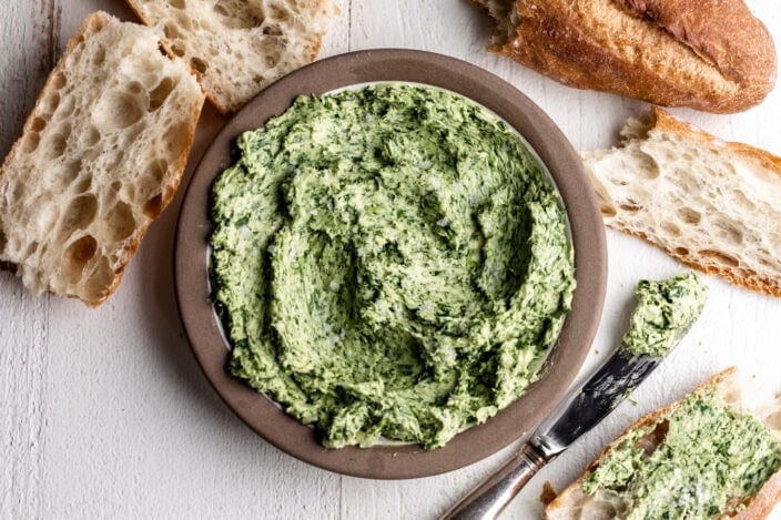 green ramps blended into butter with sliced baguette on white wood.