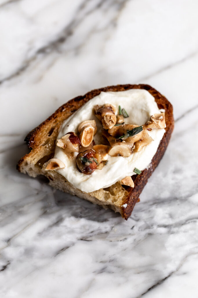 candied hazelnuts with rosemary sprinkled over whipped ricotta cheese on crusty toasted bread on marble