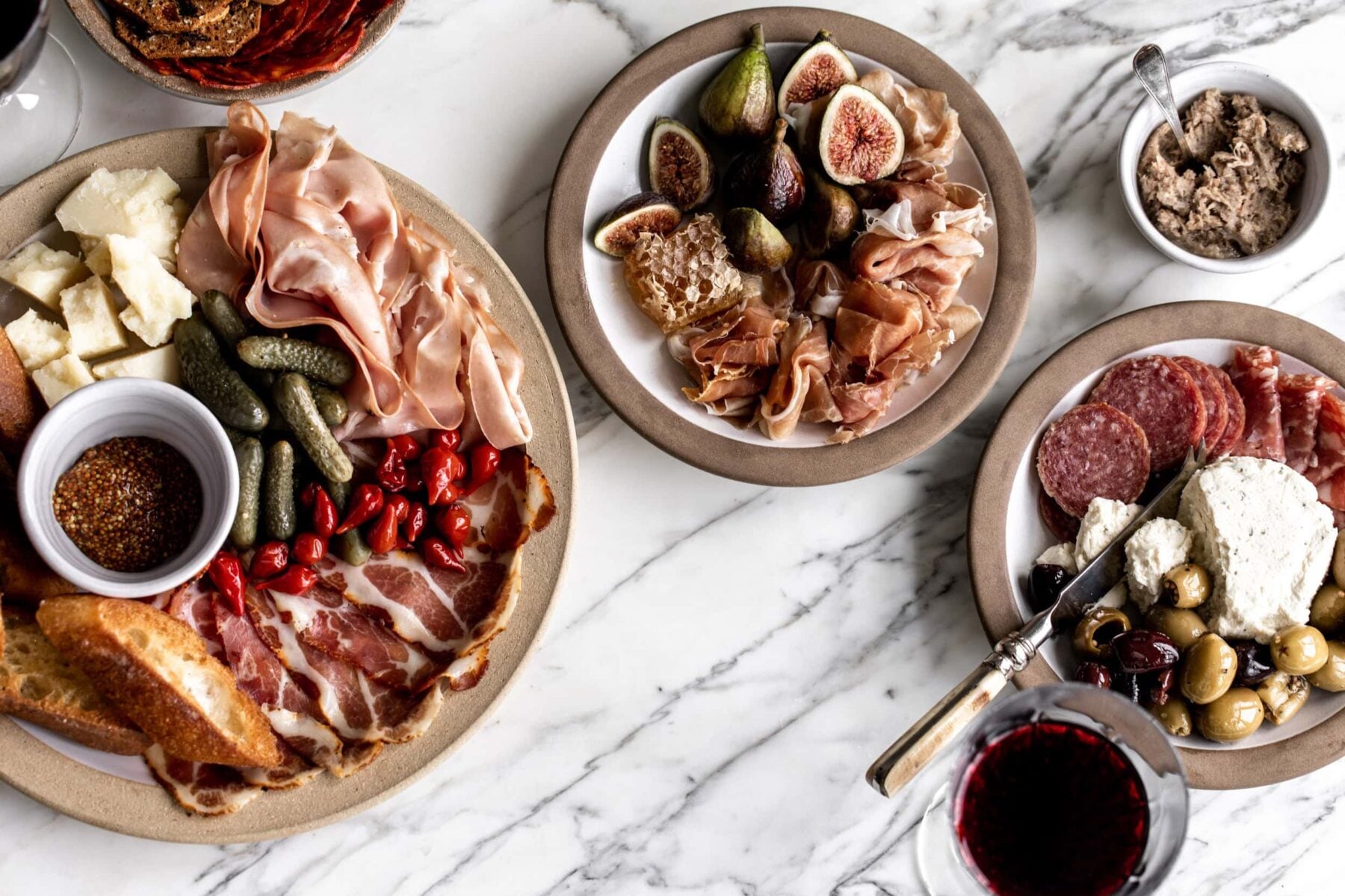 assortment of mortadella, salumi and prosciutto garnished with figs arranged on plated on a marble surface.