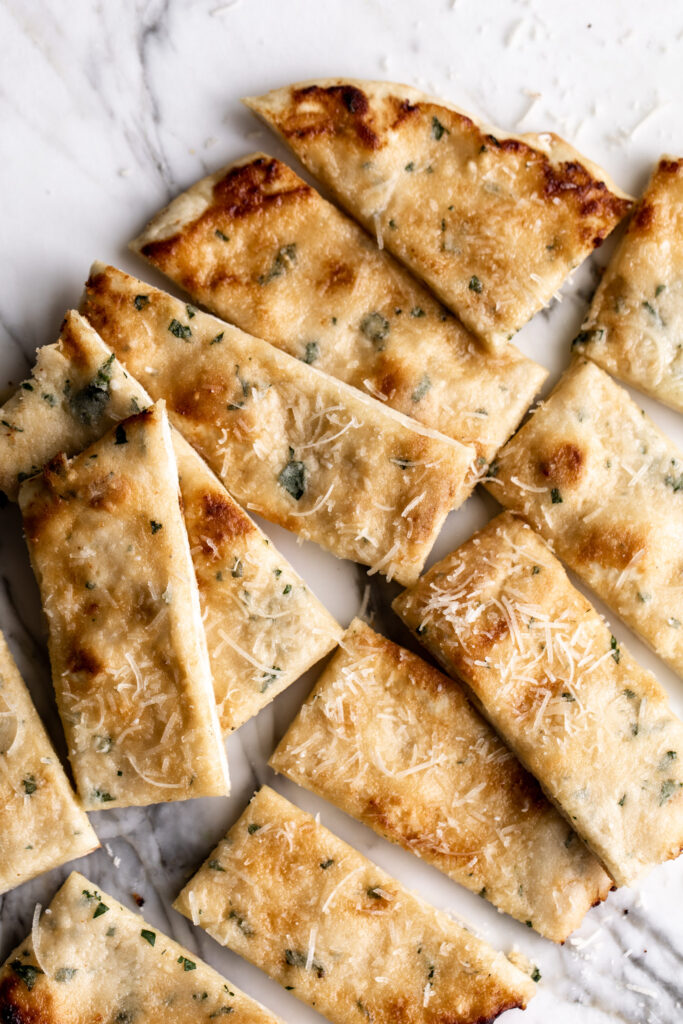 cheesy garlic flatbread with flecks of chopped parsley cut into slices on white marble