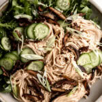 chilled buckwheat soba noodles with crispy shiitake mushrooms, slices of cucumber and green onions in a stone bowl on white wood