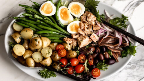 mixed greens, soft boiled eggs, green beans, tomatoes and tuna on a large serving platter for a deconstructed salad