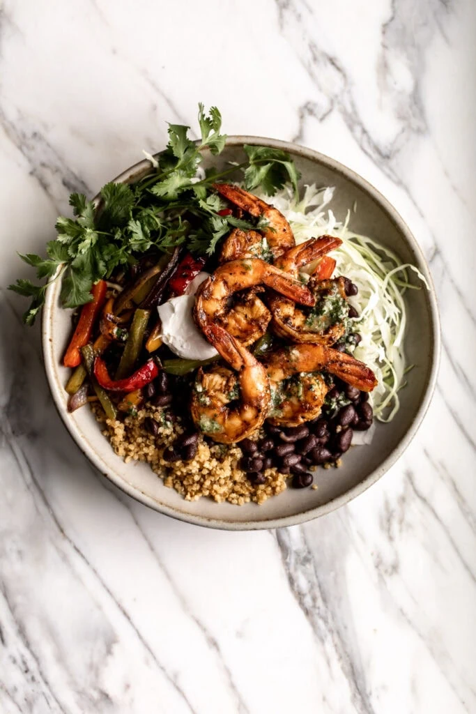 seasoned shrimp fajita bowl with sautéed peppers and onions, black beans and green cabbage in a stone bowl on a marble table