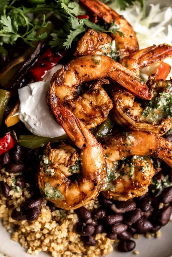 closeup image of seasoned shrimp fajitas with sautéed peppers and onions, black beans, sour cream and green cabbage in a stone bowl on a marble table
