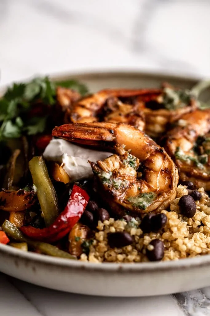 side view of seasoned shrimp fajita bowl with sautéed peppers and onions, black beans and green cabbage in a stone bowl on a marble table