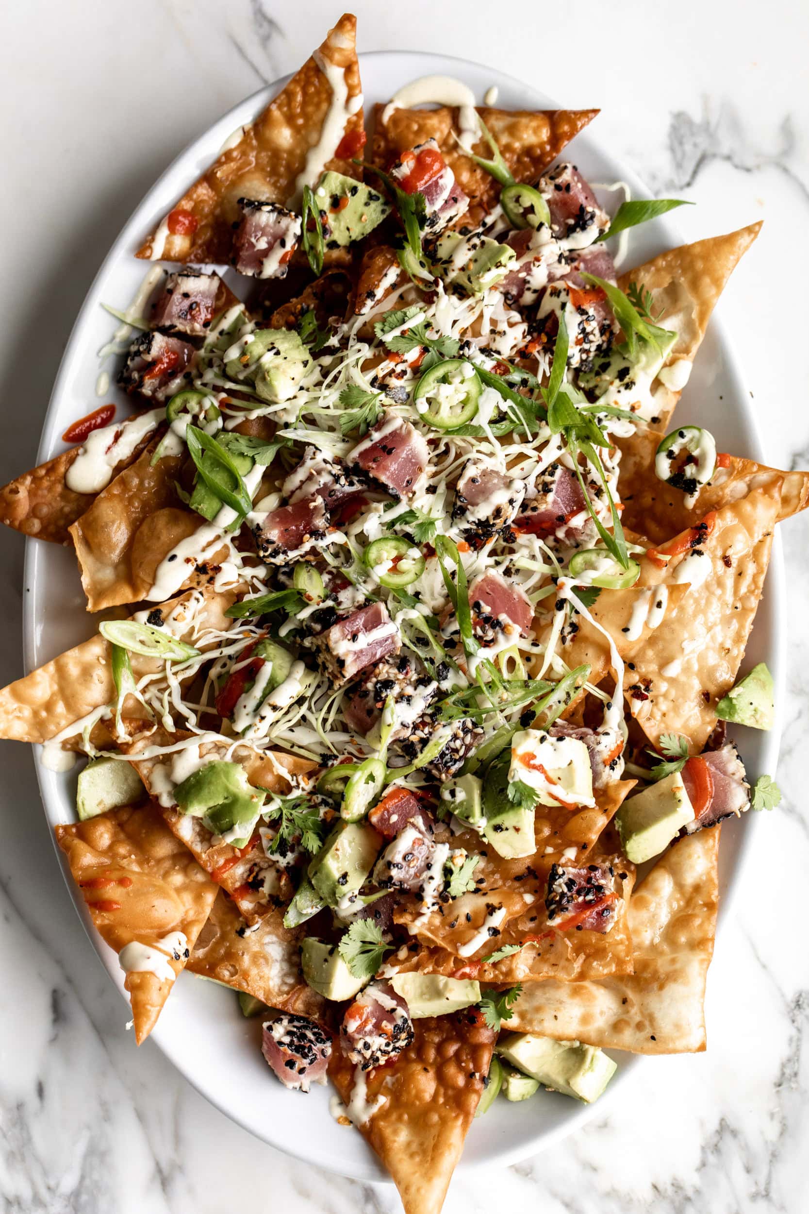 ahi tuna wonton nachos with cabbage and avocado drizzled with wasabi mayo and sriracha.