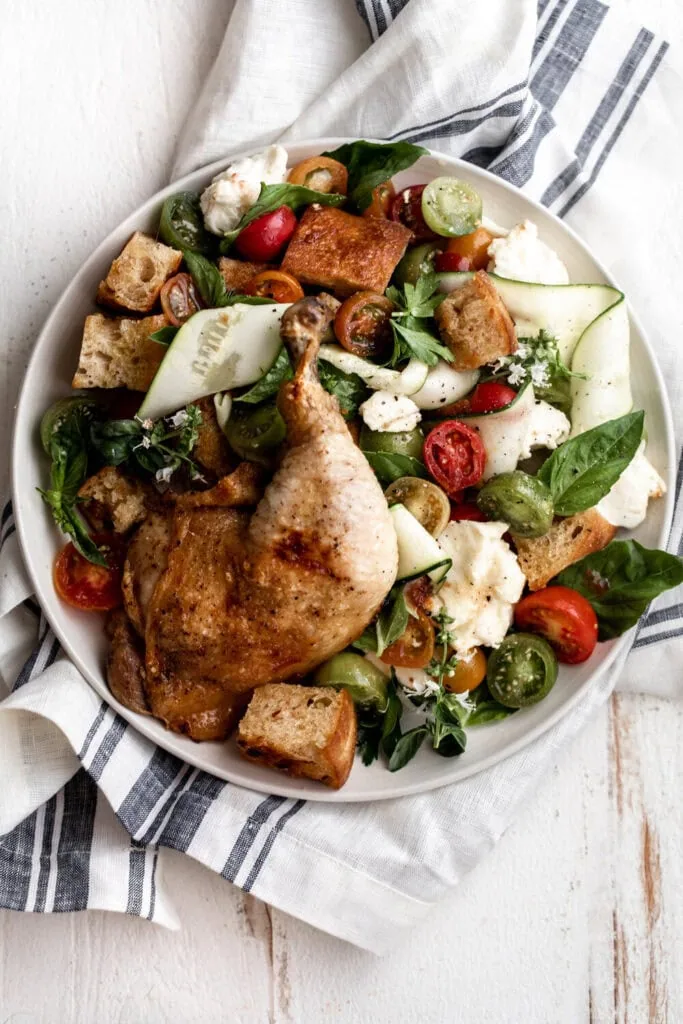 Tuscan-style panzanella salad with tomatoes, zucchini, basil and mozzarella topped with roast chicken leg