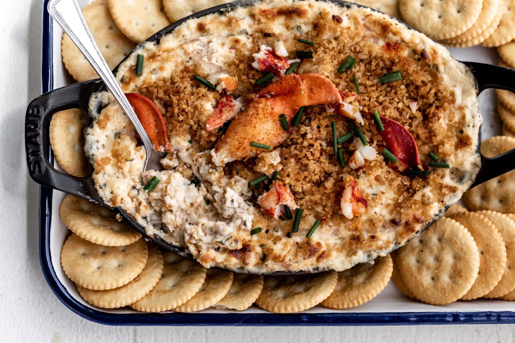 creamy baked lobster dip topped with claw meat in a black serving dish.