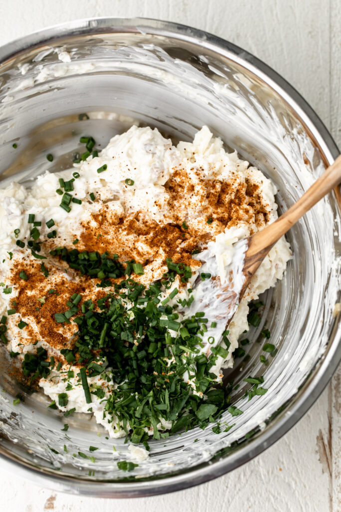 cream cheese, cheddar cheese and old bay seasoning in a metal bowl with herbs