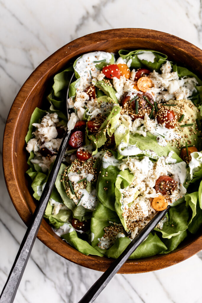 crab salad with avocado, cherry tomato, and puffed quinoa over butter lettuce in a wood bowl in a summery seafood salad