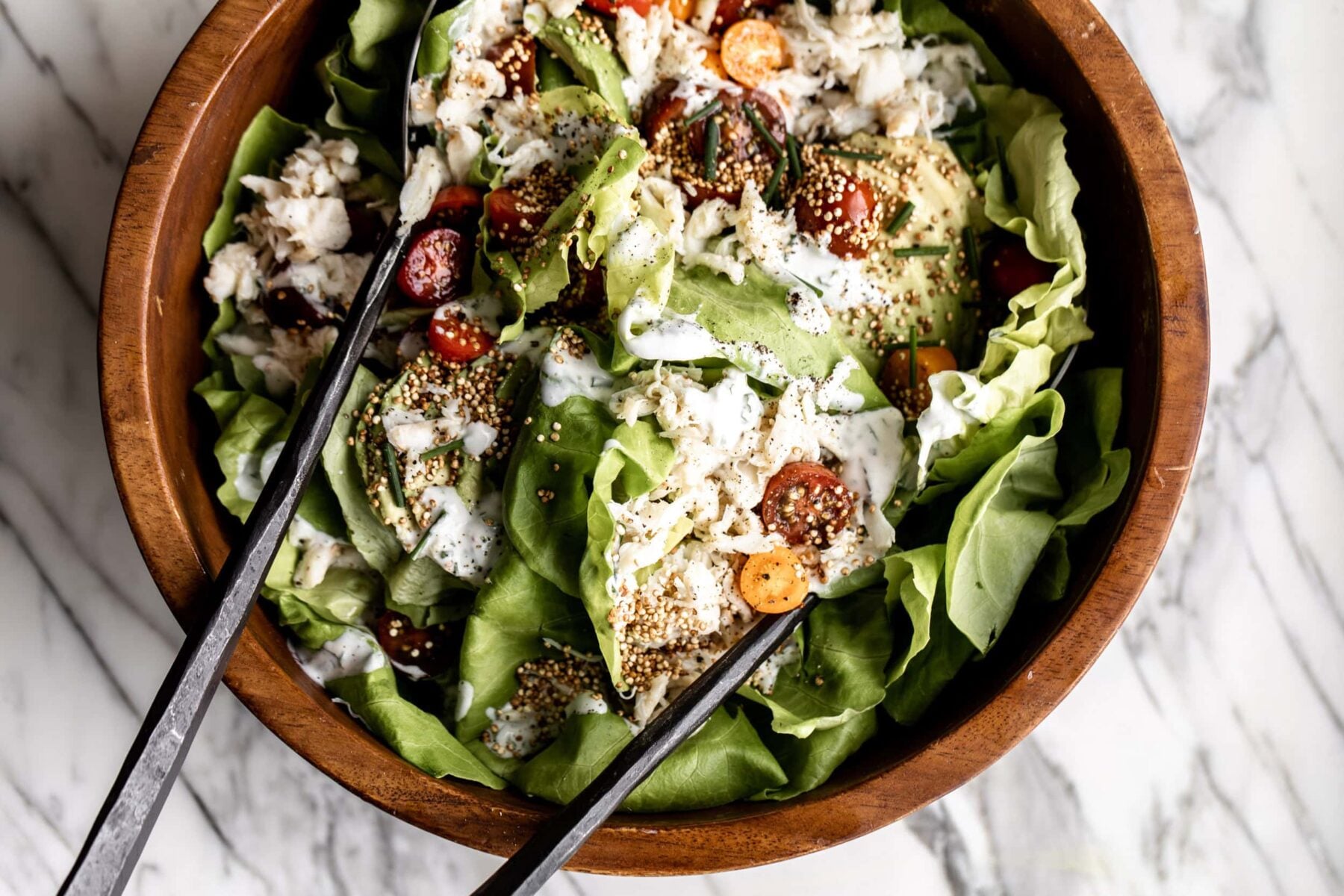 crab salad with avocado, cherry tomato, and puffed quinoa over butter lettuce in a wood bowl.