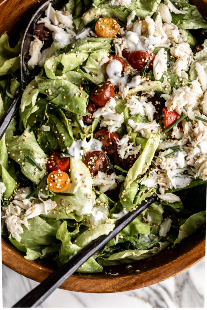 crab salad with avocado, cherry tomato, and puffed quinoa over butter lettuce in a wood bowl