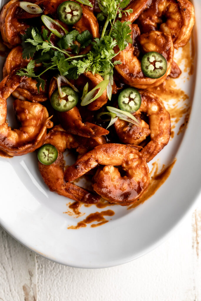 shrimp diablo cooked in a tomato and chili sauce topped with diced green onion and cilantro on a white serving platter