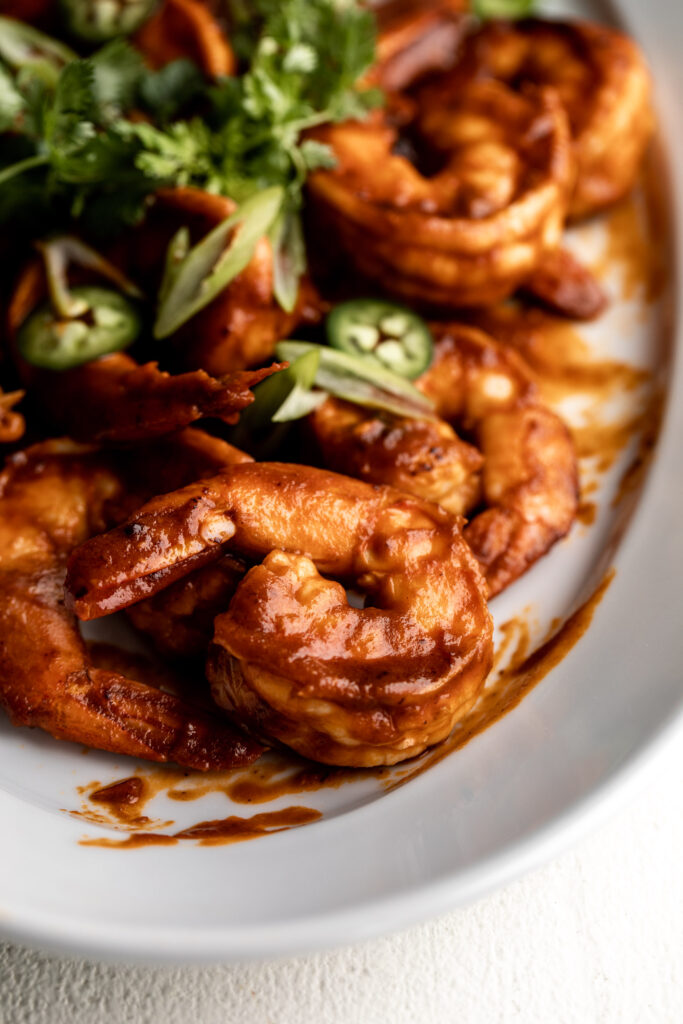 closeup photo of shrimp diablo cooked in a tomato and chili sauce topped with diced green onion and cilantro on a white serving platter