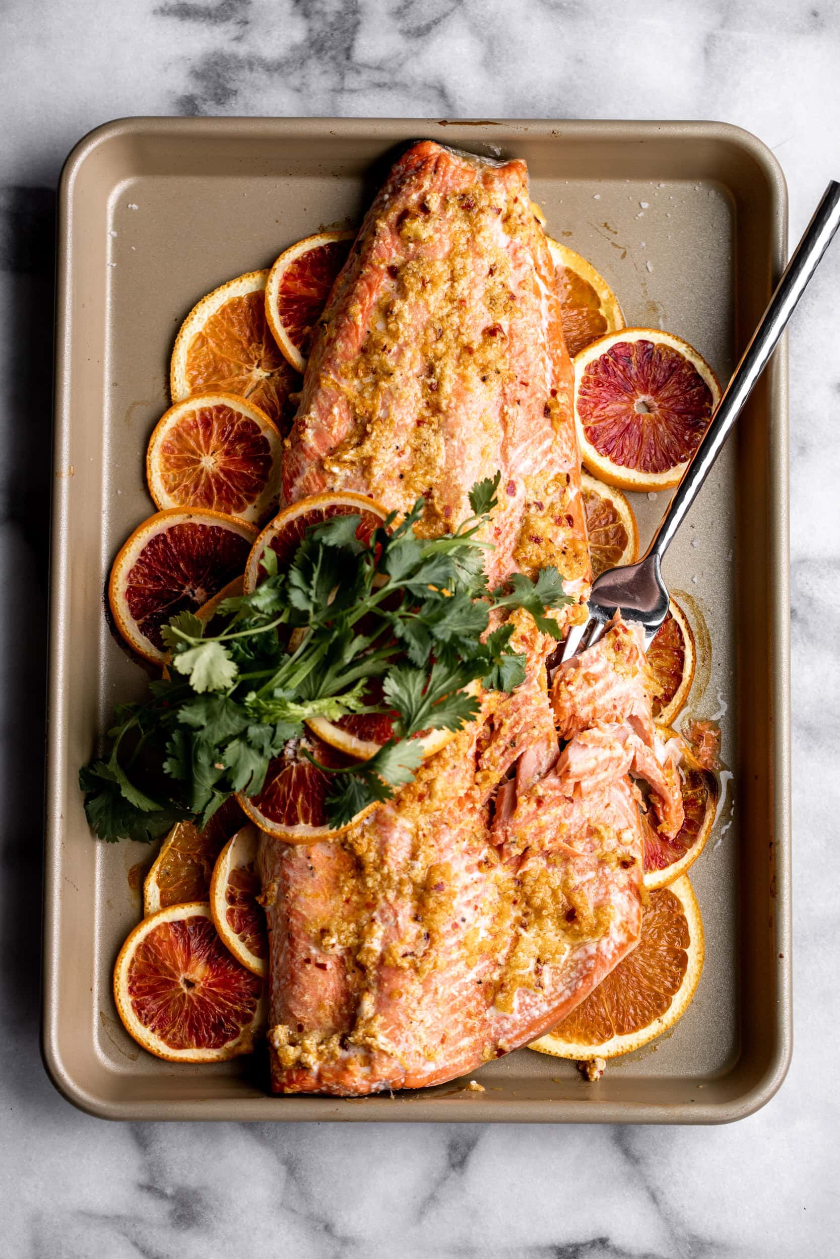 roasted orange ginger salmon half salmon with orange slices and cilantro sprigs.