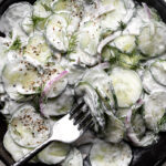 creamy cucumber salad with sour cream sauce, dill and red onion in black stone bowl