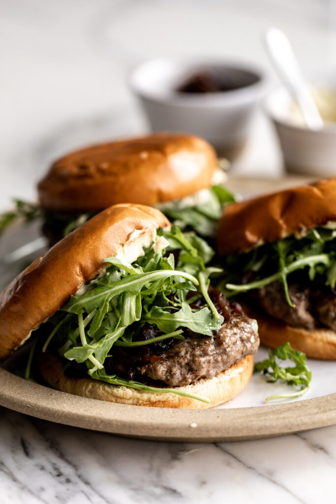 Lamb burgers made using ground New Zealand lamb served on brioche buns with arugula, caramelized onions and homemade curry mayonnaise on a plate