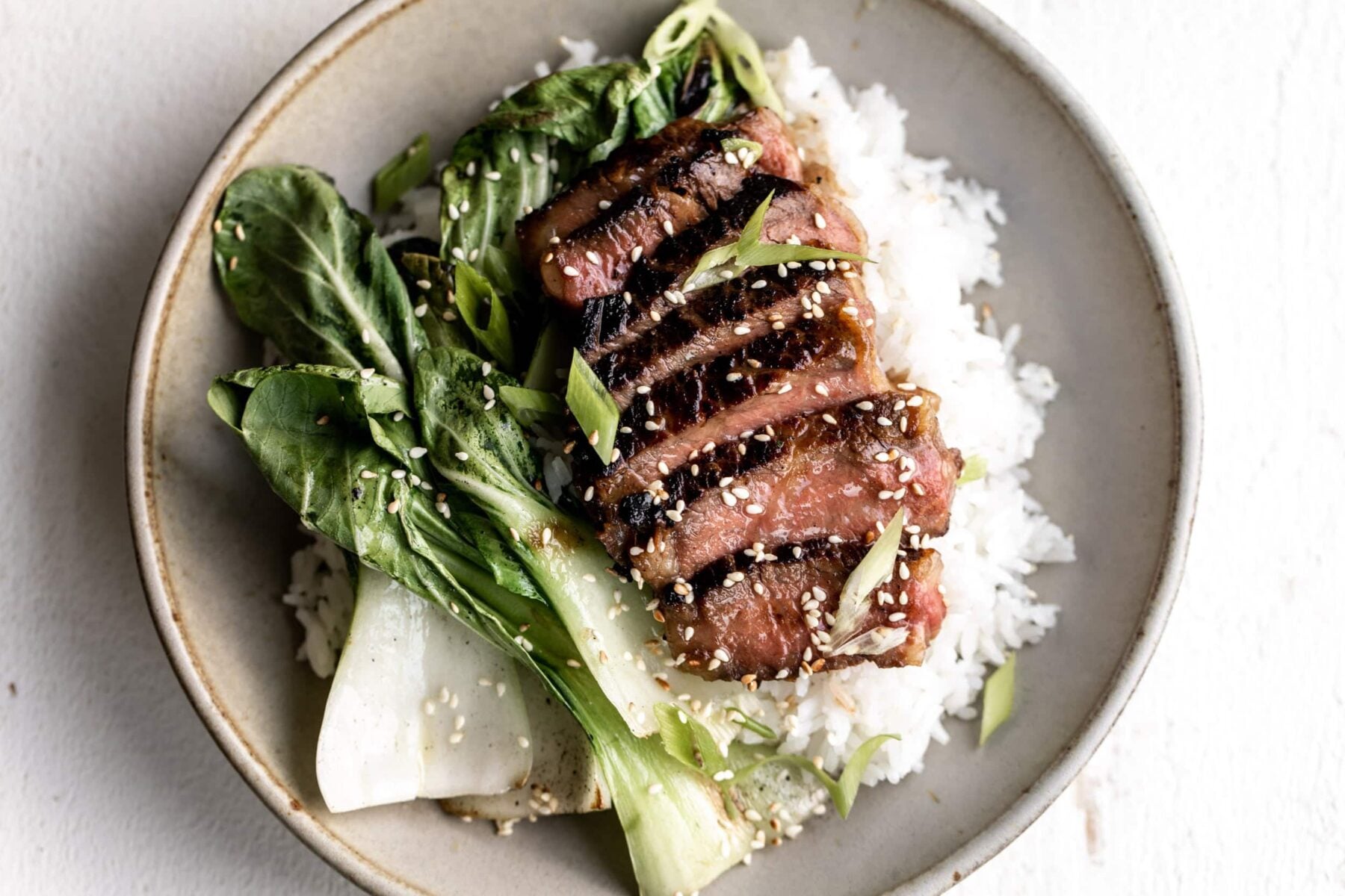 New Zealand beef miso marinated ribeye over white rice with bok choy in bowl.