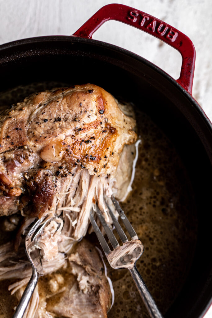 braised pulled pork with fork in dutch oven