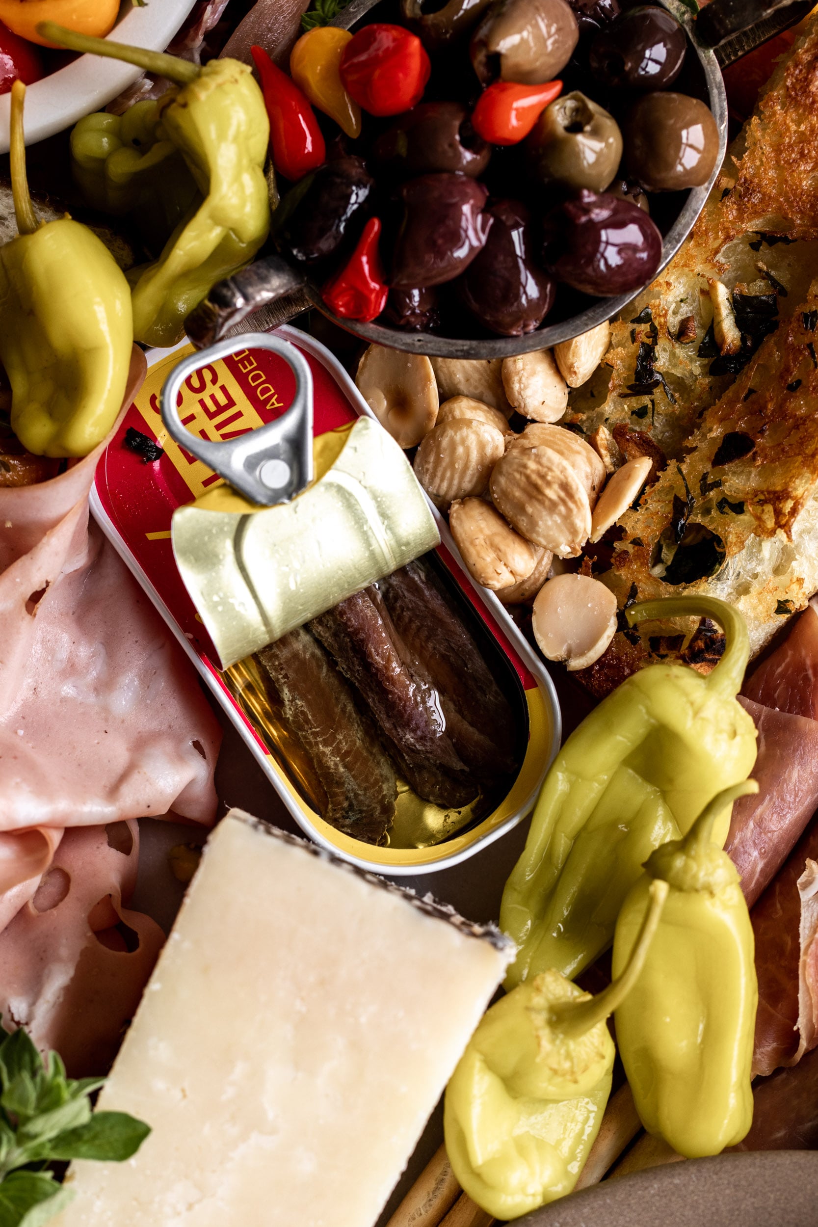 anchovy tin opened with Pepperoncini peppers and olives in small bowl.