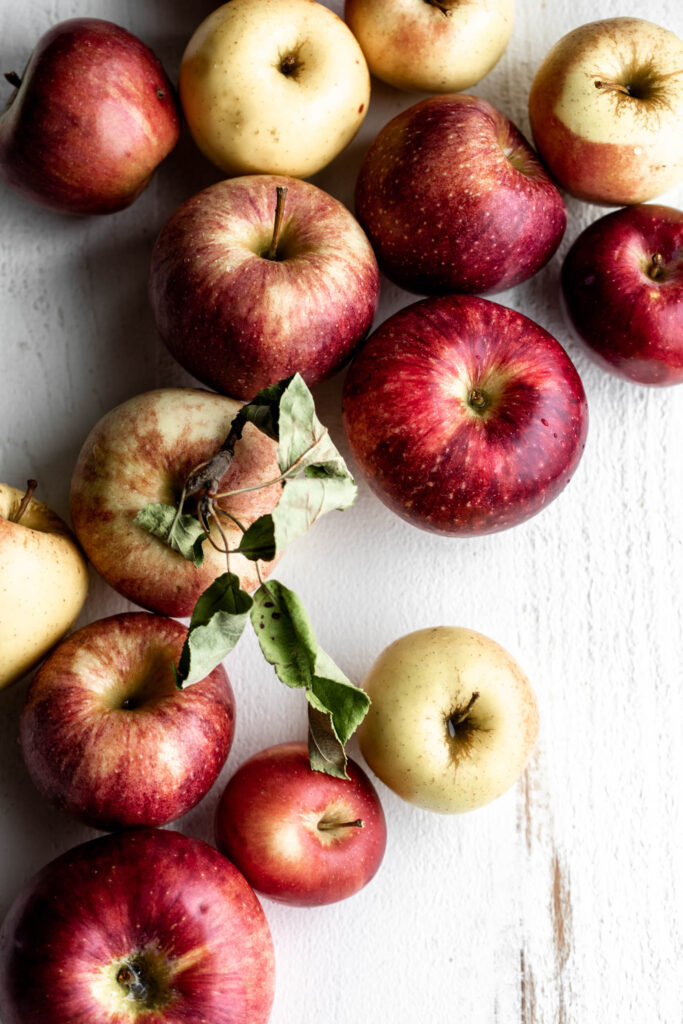 A variety of apples picked at an orchard on a white wood board