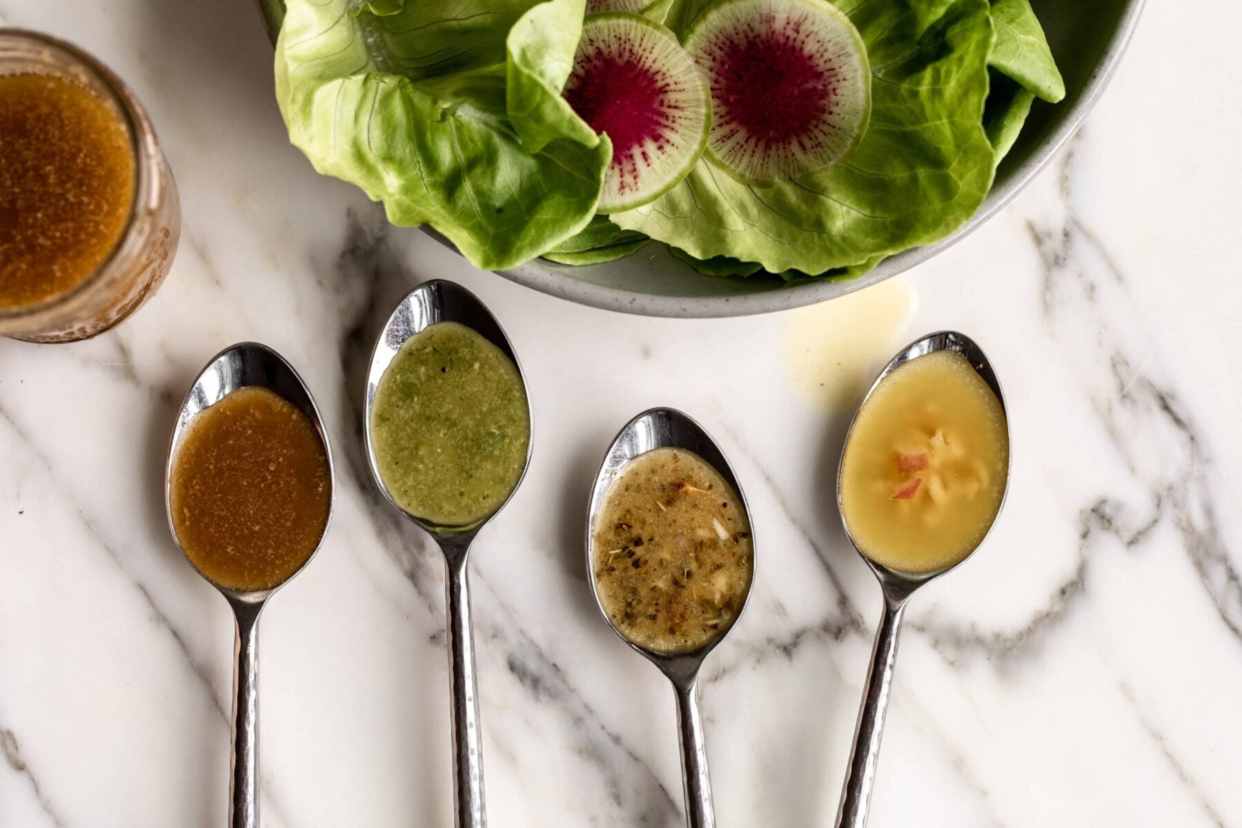 4 types of basic vinaigrette on spoons with butter lettuce salad.