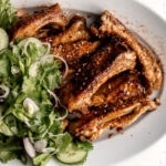 baked pork ribs broiled and topped with sesame seeds and togarashi with cucumber green onion shallot and cilantro on a white platter