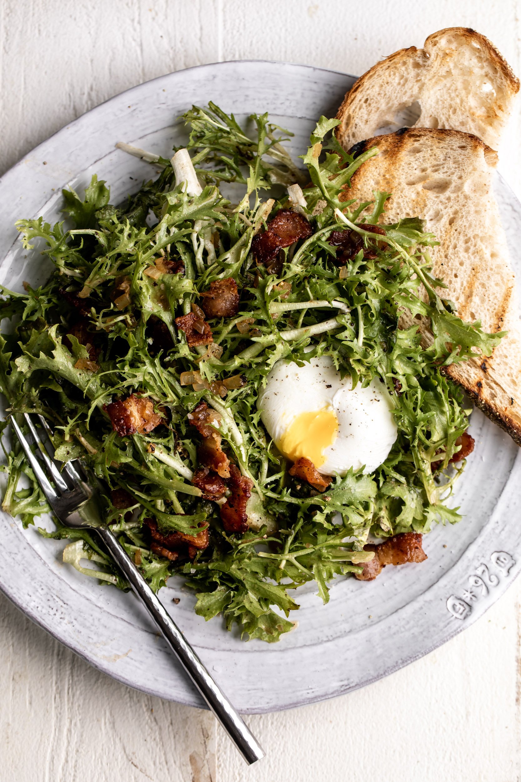 bacon and frisée French salad with a poached egg split open on a rustic plate.