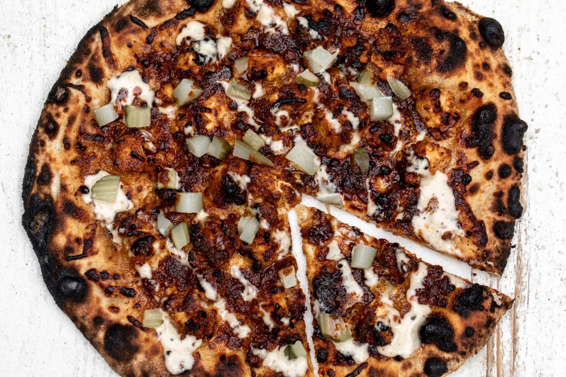 nashville hot chicken pizza topped with fried chicken a drizzle of alabama white sauce with chopped pickles.